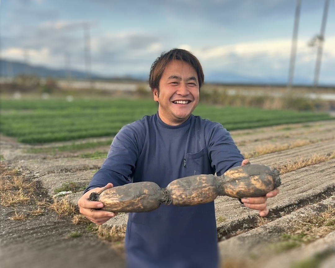 畑で収穫物を手に笑顔を見せる生産者